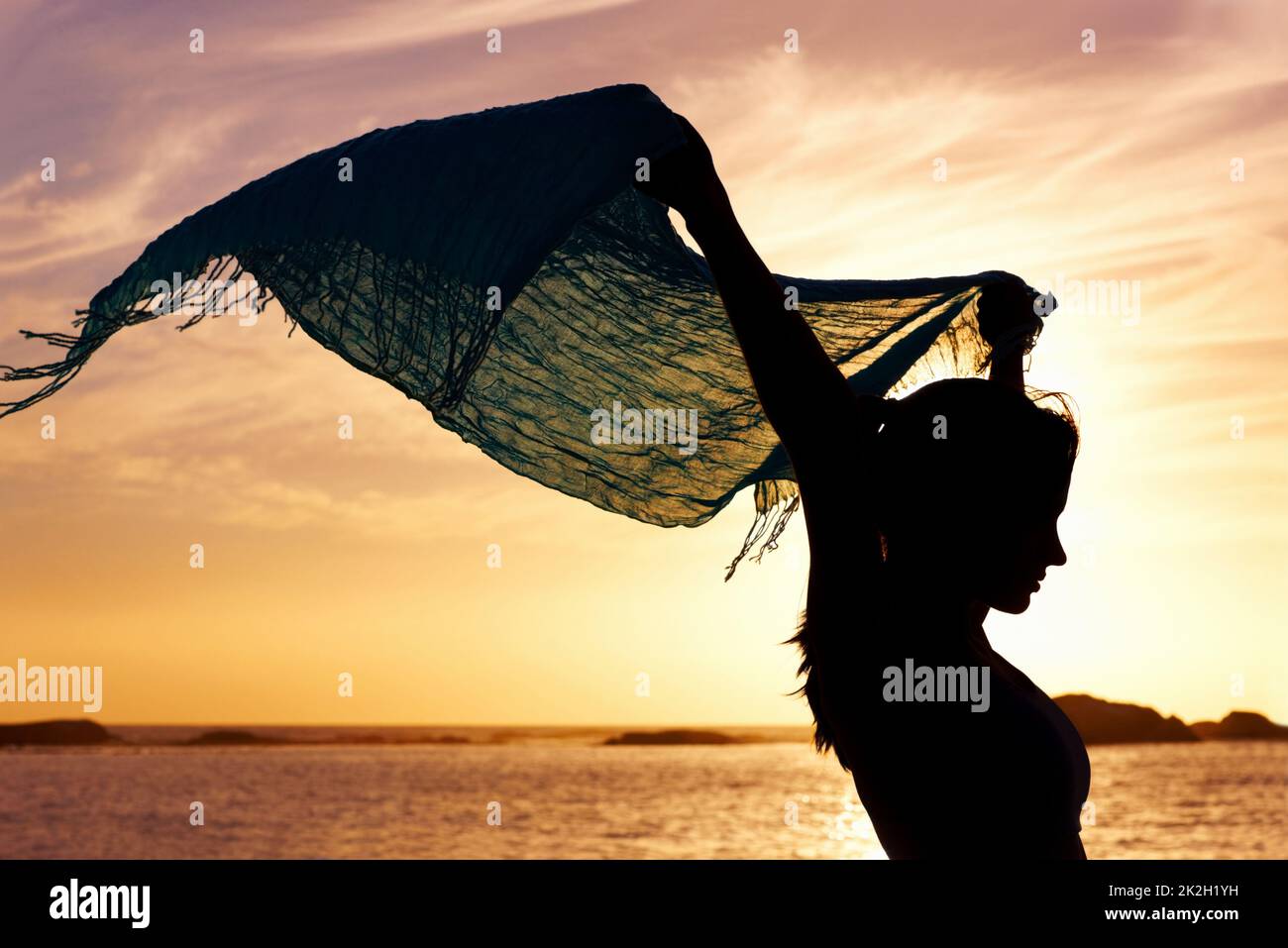 Silhouette image of a woman holding up shawl at sunset. Silhouette image of a beautiful woman holding up shawl at sunset. Stock Photo