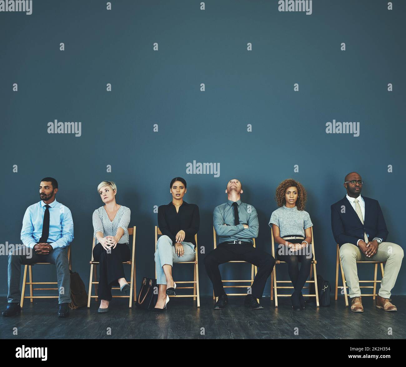 Consider everything a test, even the possible extended 10-minute wait. Shot of a group of well-dressed business people seated in line while waiting to be interview. Stock Photo