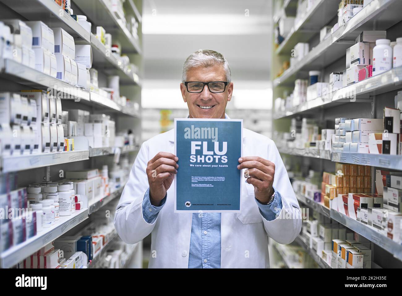 Hes got your medication covered. Portrait of a mature male pharmacist holding up a sign indicating that you can get flu shots there. Stock Photo