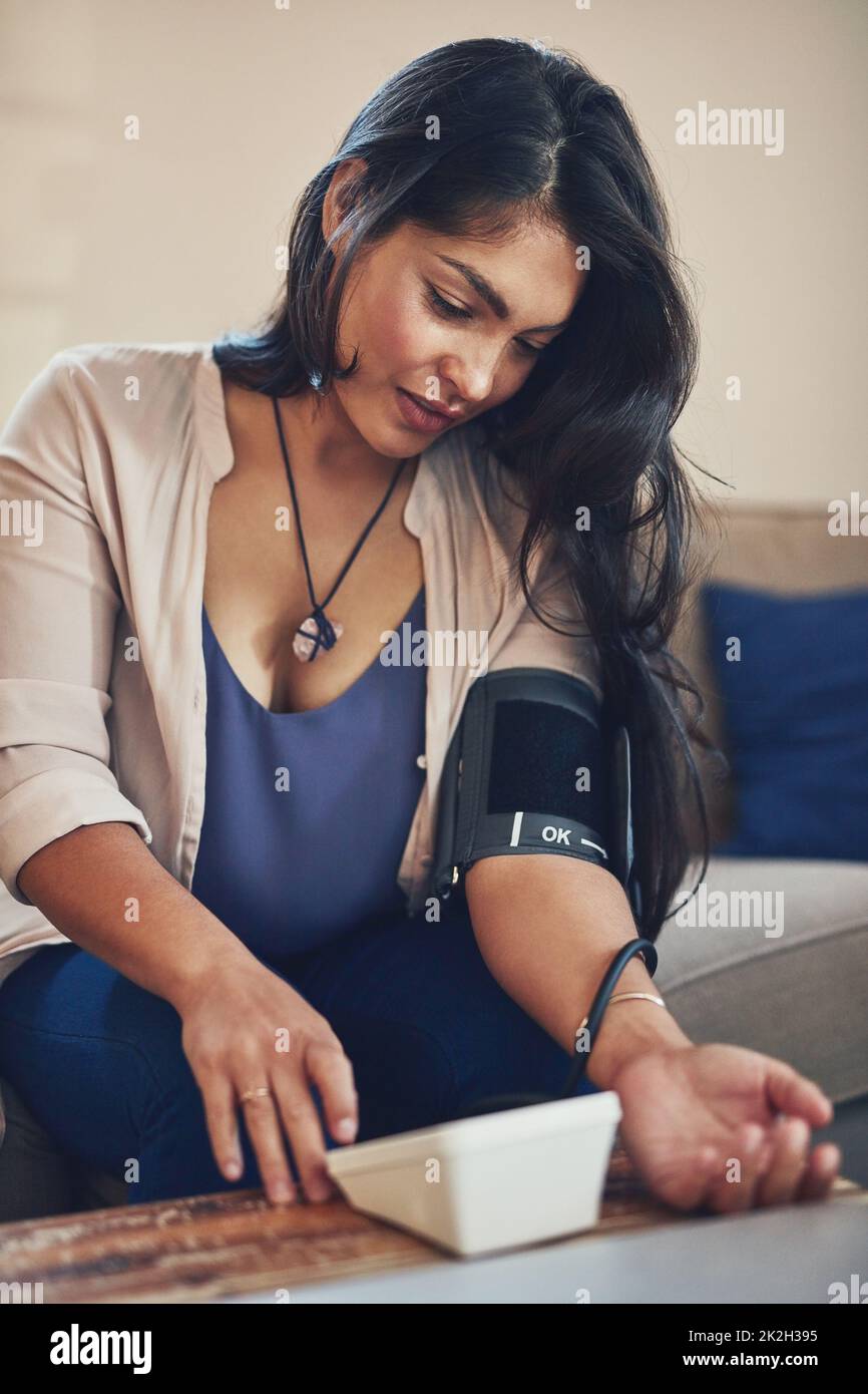 Maintaining stable blood pressure levels. Shot of a young woman checking her blood pressure at home. Stock Photo