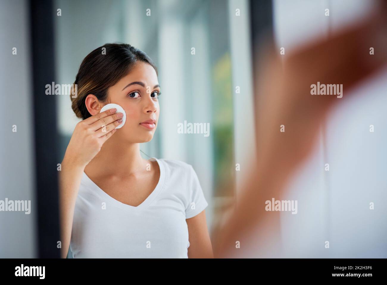 Caring for her vibrantly soft skin. Shot of an attractive young woman cleaning her face with cotton wool in the bathroom. Stock Photo