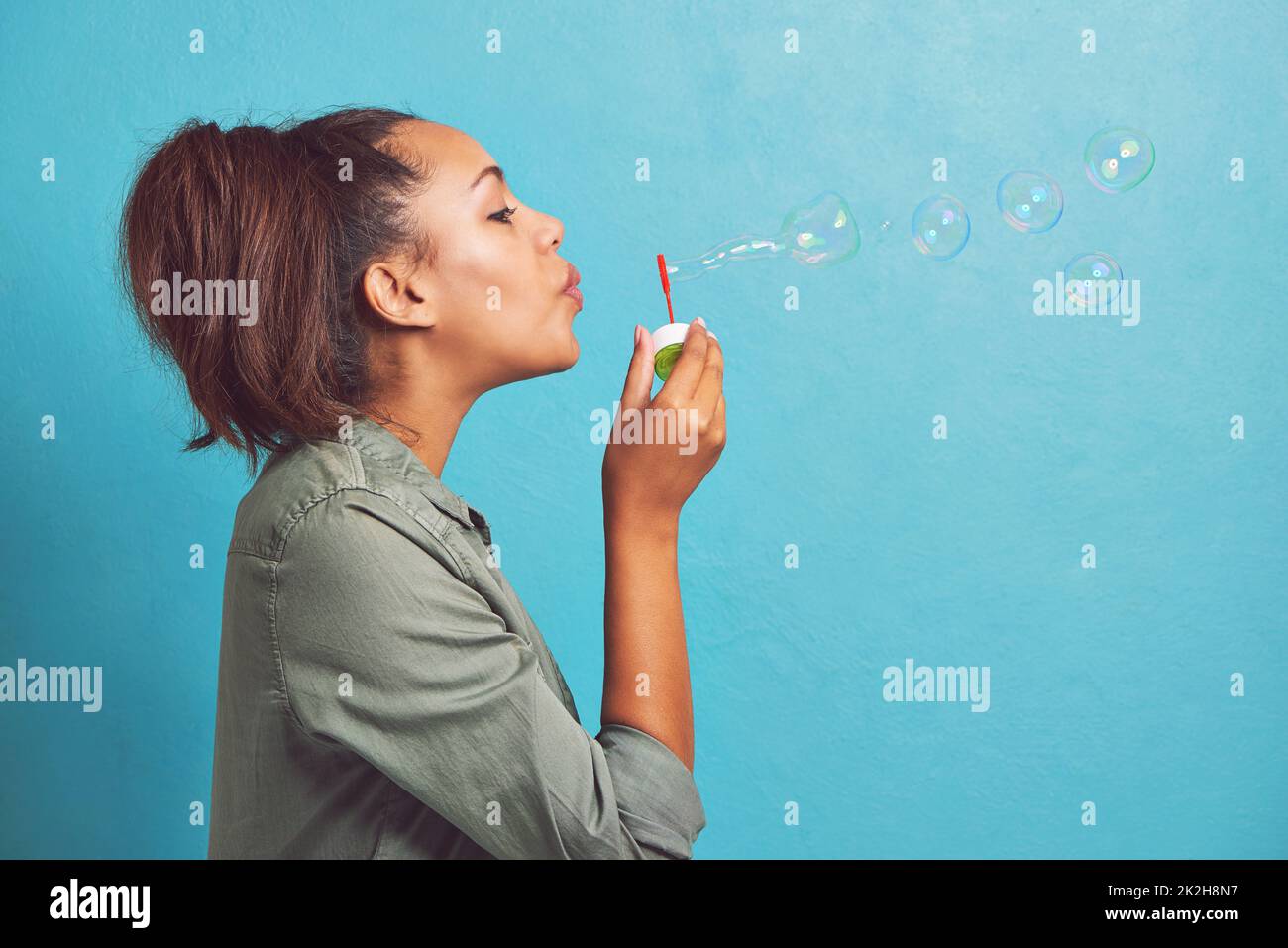 Keep calm and blow bubbles. Cropped shot of a young woman blowing bubbles against a blue background. Stock Photo