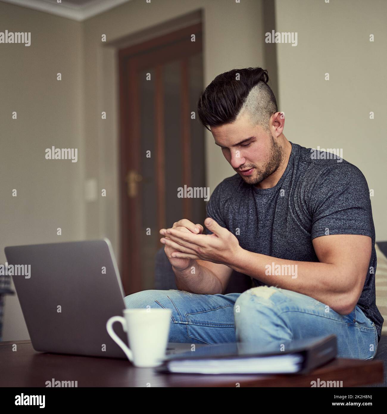 Memo remember to buy a notebook. Shot of a serious young man making notes on his hand while he works on his laptop at home. Stock Photo