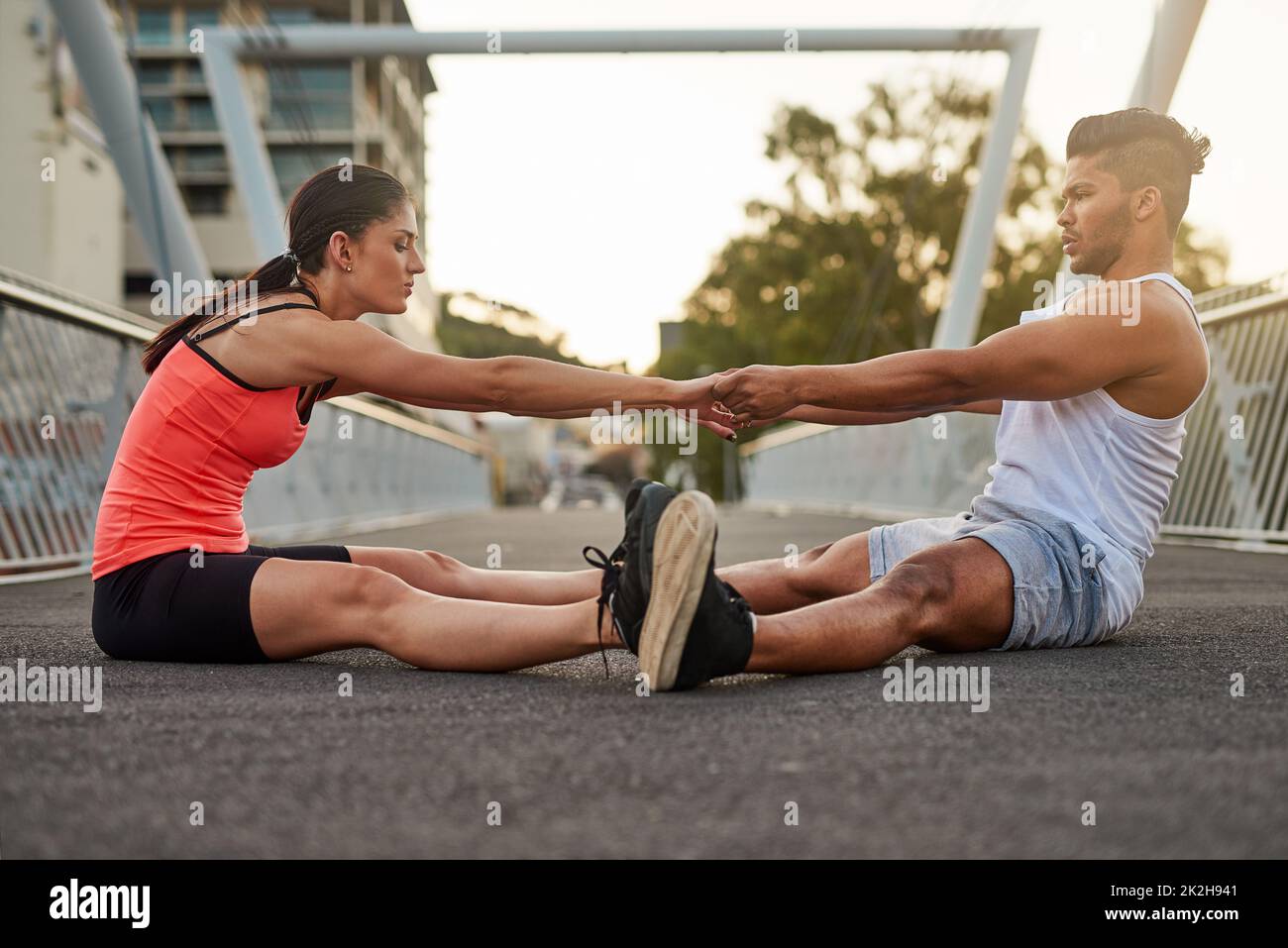 Lemme give you a hand. Shot of a young couple warming up on a bridge before their workout. Stock Photo