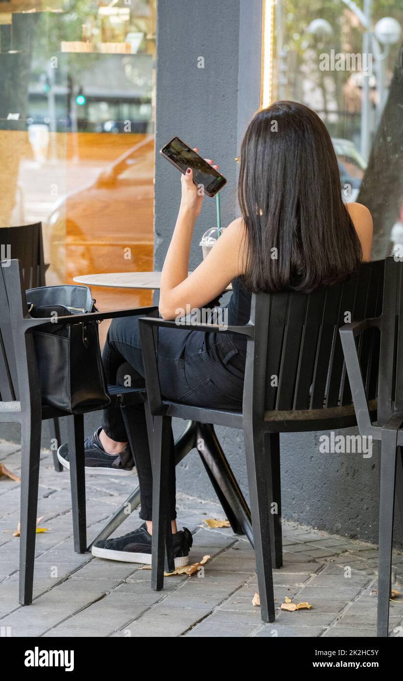 Young girl talking on phone from abroad with her family or friend, holding smartphone speaking, sitting at table  Stock Photo