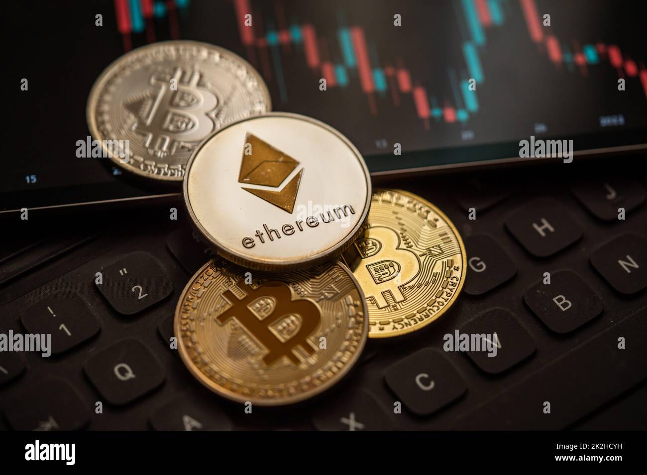 Gold Bitcoin and Ethereum cryptocurrency coins with candle stick graph chart, laptop keyboard, and digital background. Stock Photo