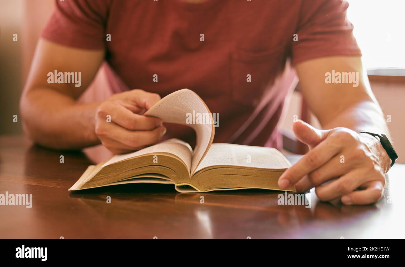 Praying is important for peace of mind. Shot of a young man sitting at a table reading his bible. Stock Photo