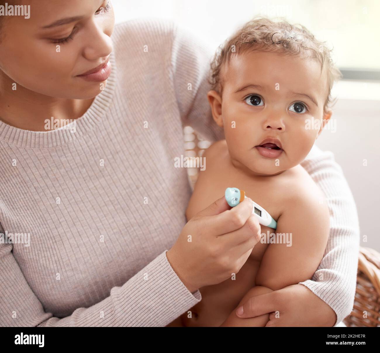 You feel a bit warm to me. Shot of a baby crying while having her temperature checked by her mother. Stock Photo