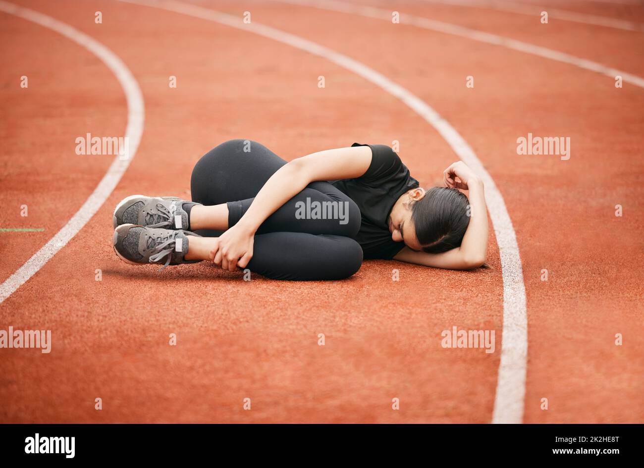 Someone bring me an ice pack. Shot of an athletic young woman suffering from a sports injury while out on the track. Stock Photo