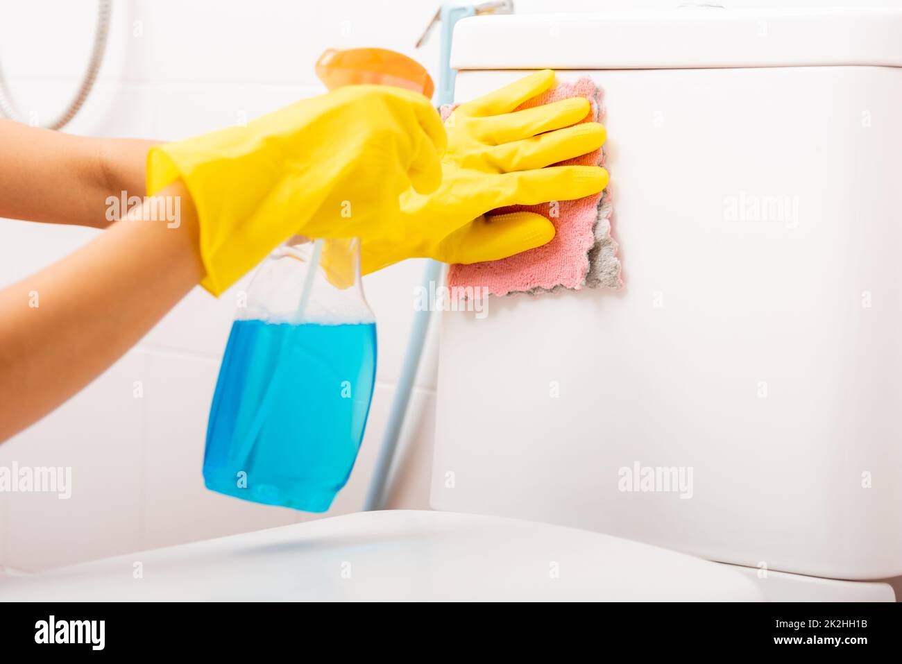 Hand of Asian woman cleaning toilet seat using liquid spray and pink