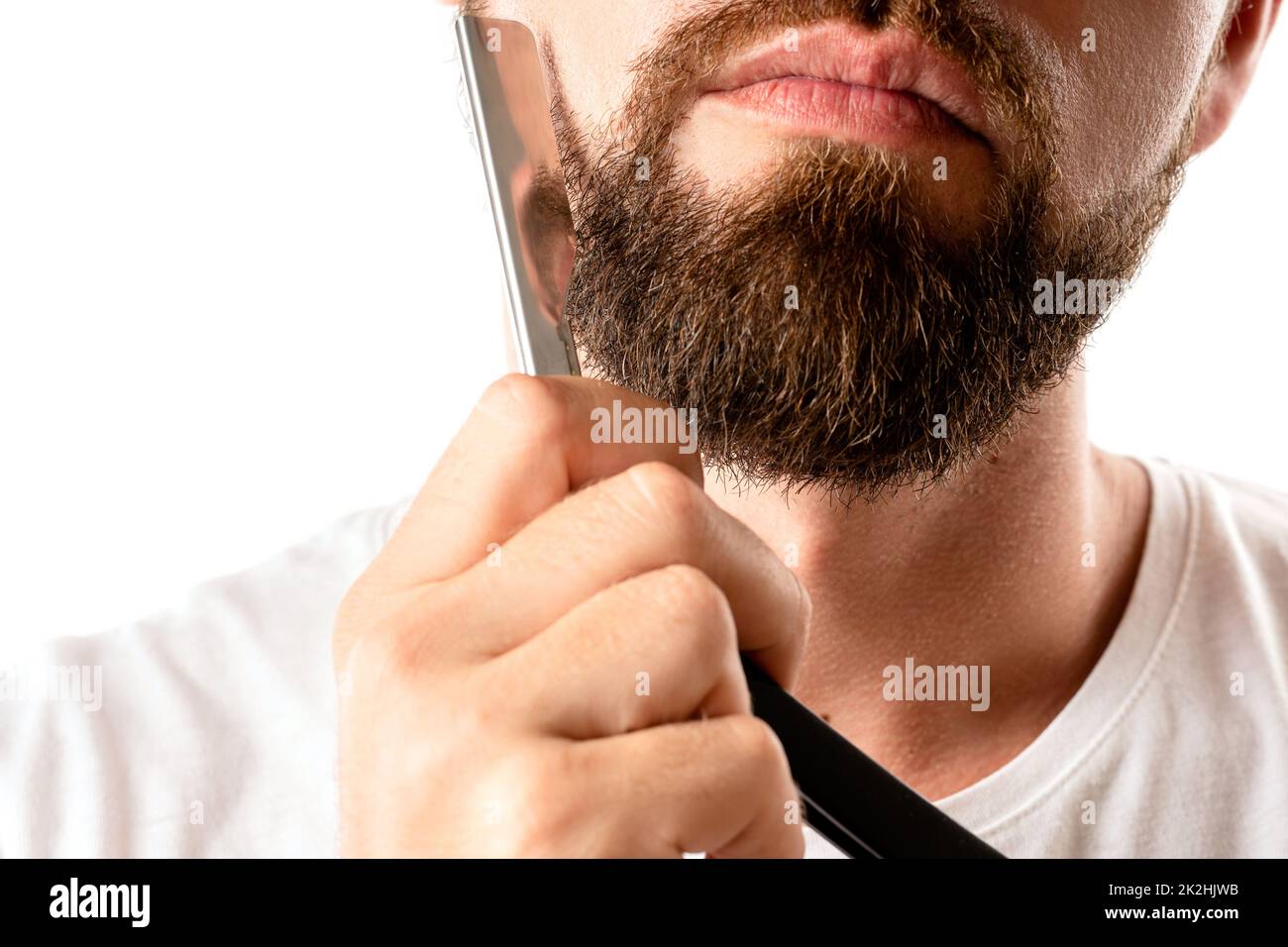 Man is shaving his thick beard with a straight razor Stock Photo