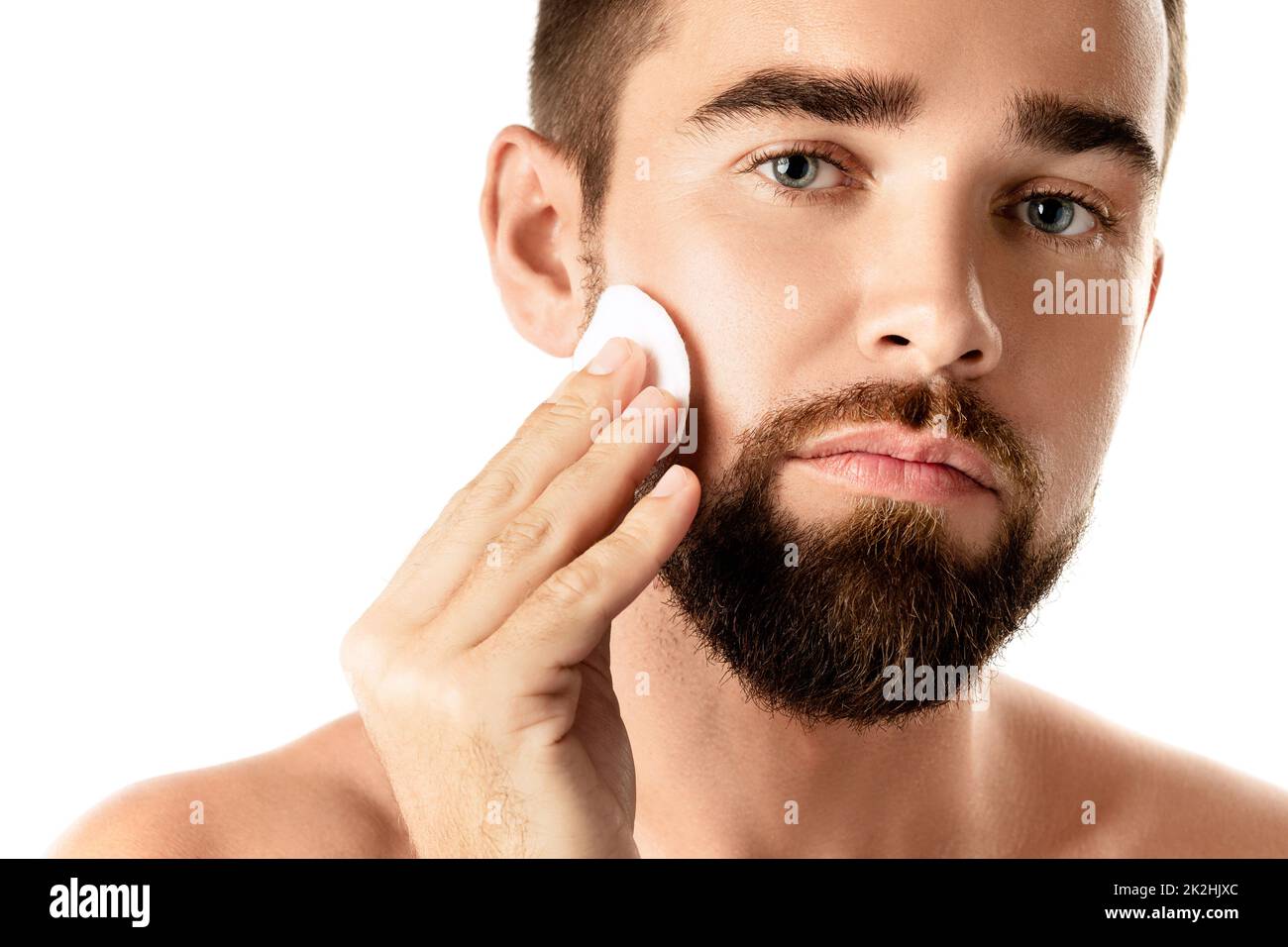 Young handsome man is cleaning his face with a cotton pad Stock Photo