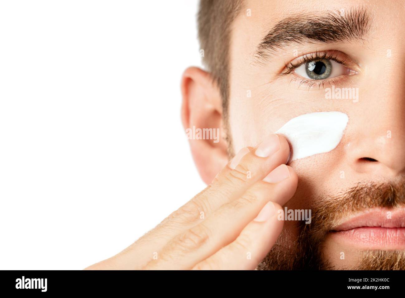 Young man is applying moisturizing and anti aging cream on his face Stock Photo