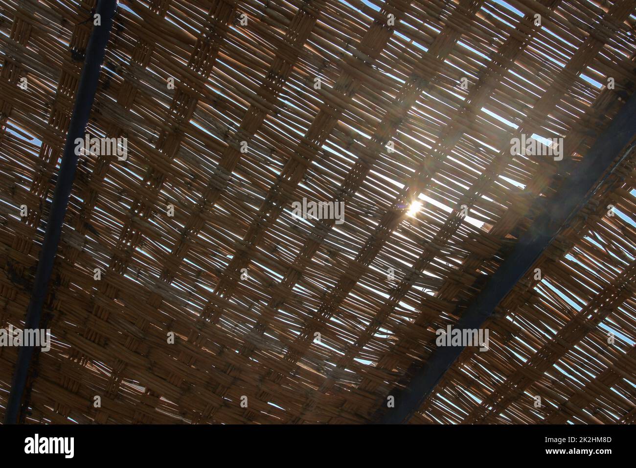 View through palm leaves roof, sun shining behind. Abstract tropical background. Stock Photo