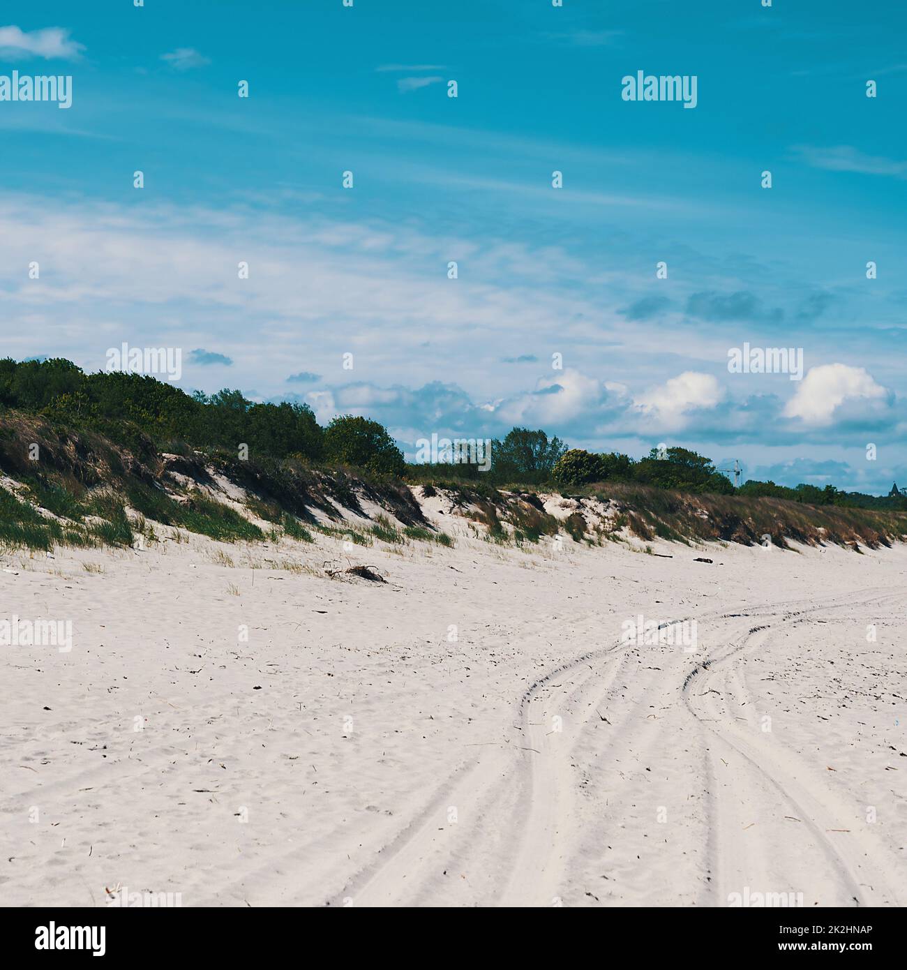 Dunes, overgrown with grass in places, car tracks on the sand. Blue sky with clouds Stock Photo