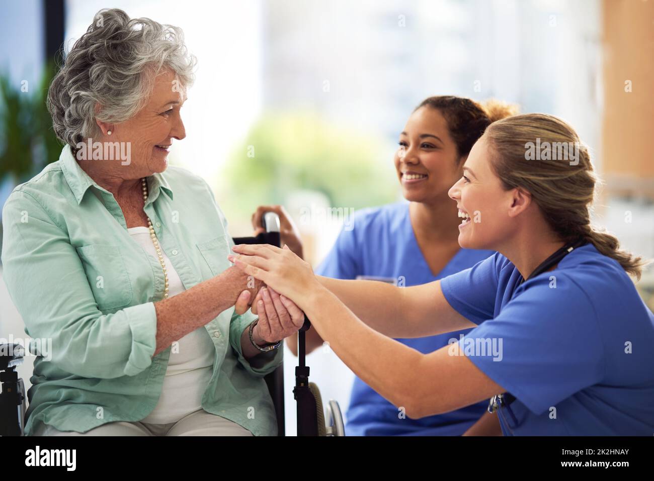 Shot of a smiling female doctor and nurse talking with a senior woman in a wheelchair Stock Photo