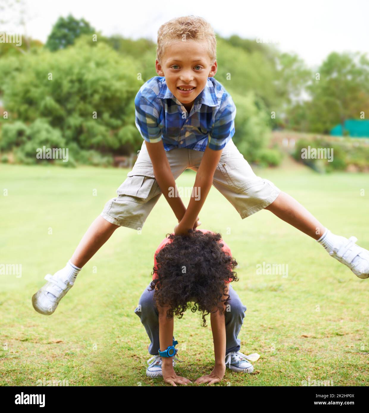 Leapfrogging. A young boy doing a leapfrog over his friend's back. Stock Photo
