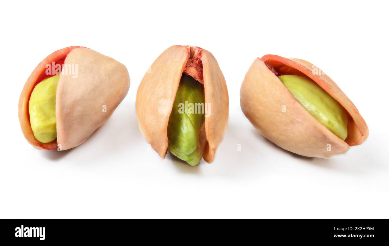 Three red turkish pistachios, peeled green nuts visible in cracked shells isolated on white background. Stock Photo