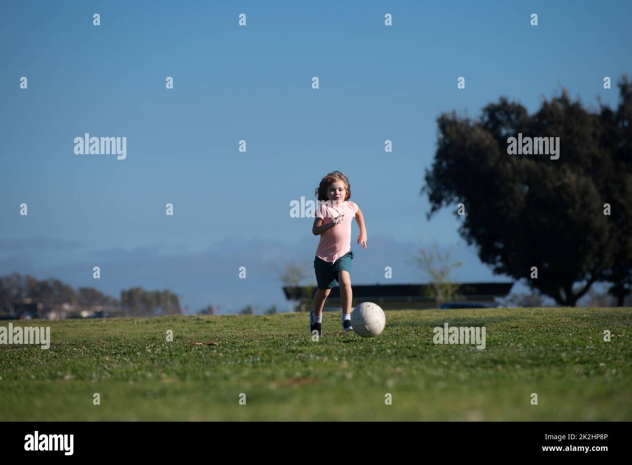 Excited child boy kicking ball in the grass outdoors. Soccer kids, children play football. Kids training soccer. Stock Photo
