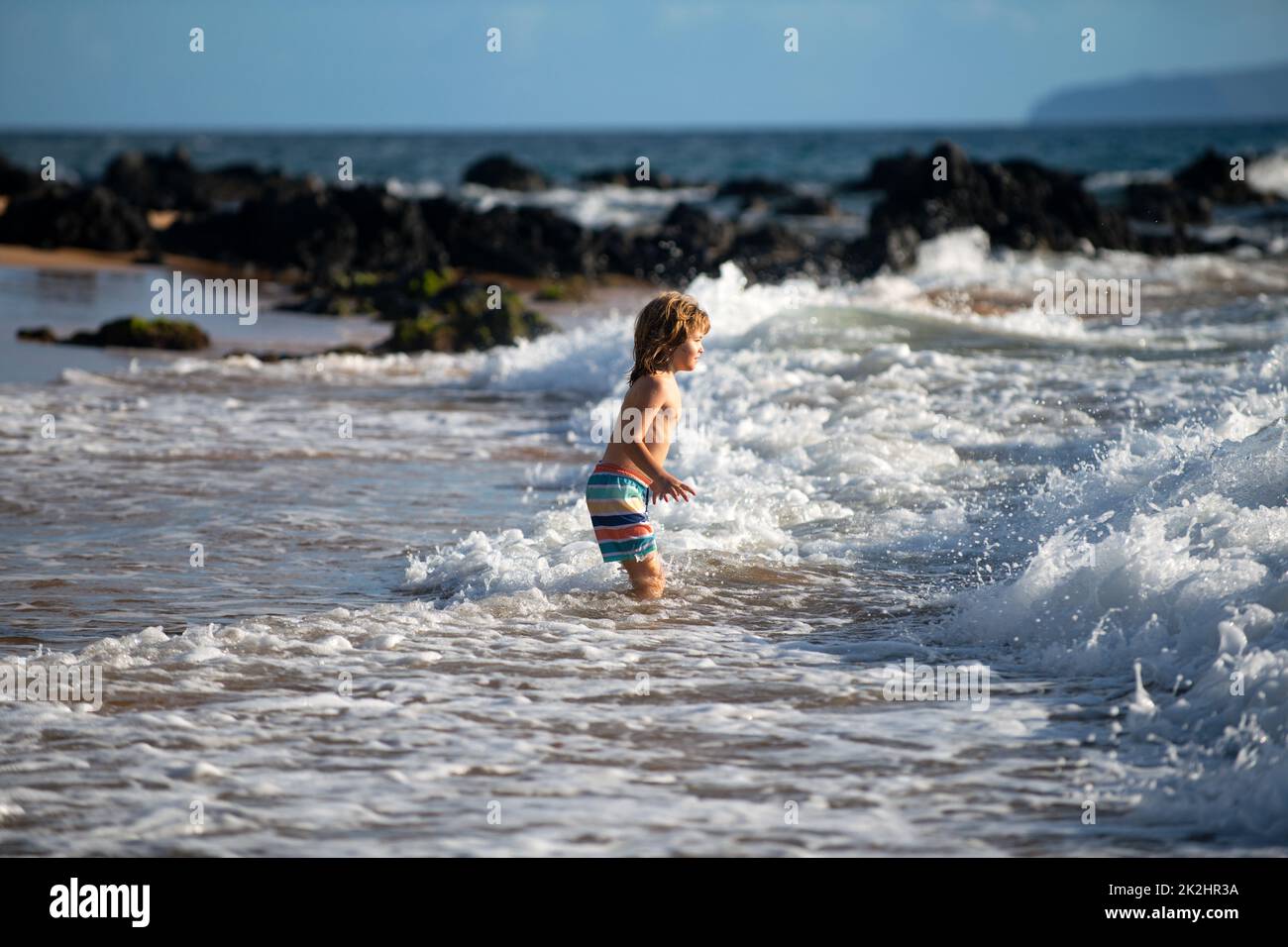 Boy kid jumping in sea waves. Jump by water sea splashes. Summer kids vacation. Stock Photo