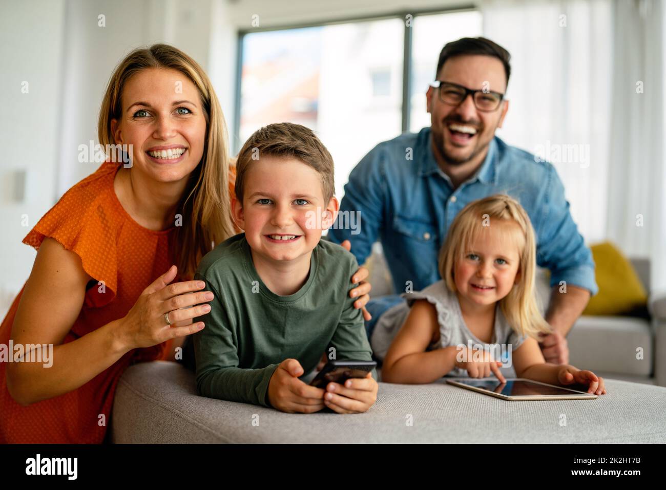 Happy young family having fun time at home. Parents with children using digital device. Stock Photo