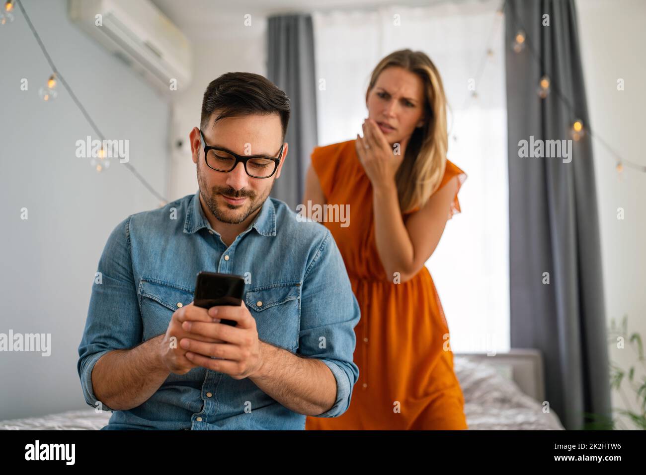 Jealous woman spying boyfriend and watching his mobile phone. Couple cheating jealousy concept Stock Photo