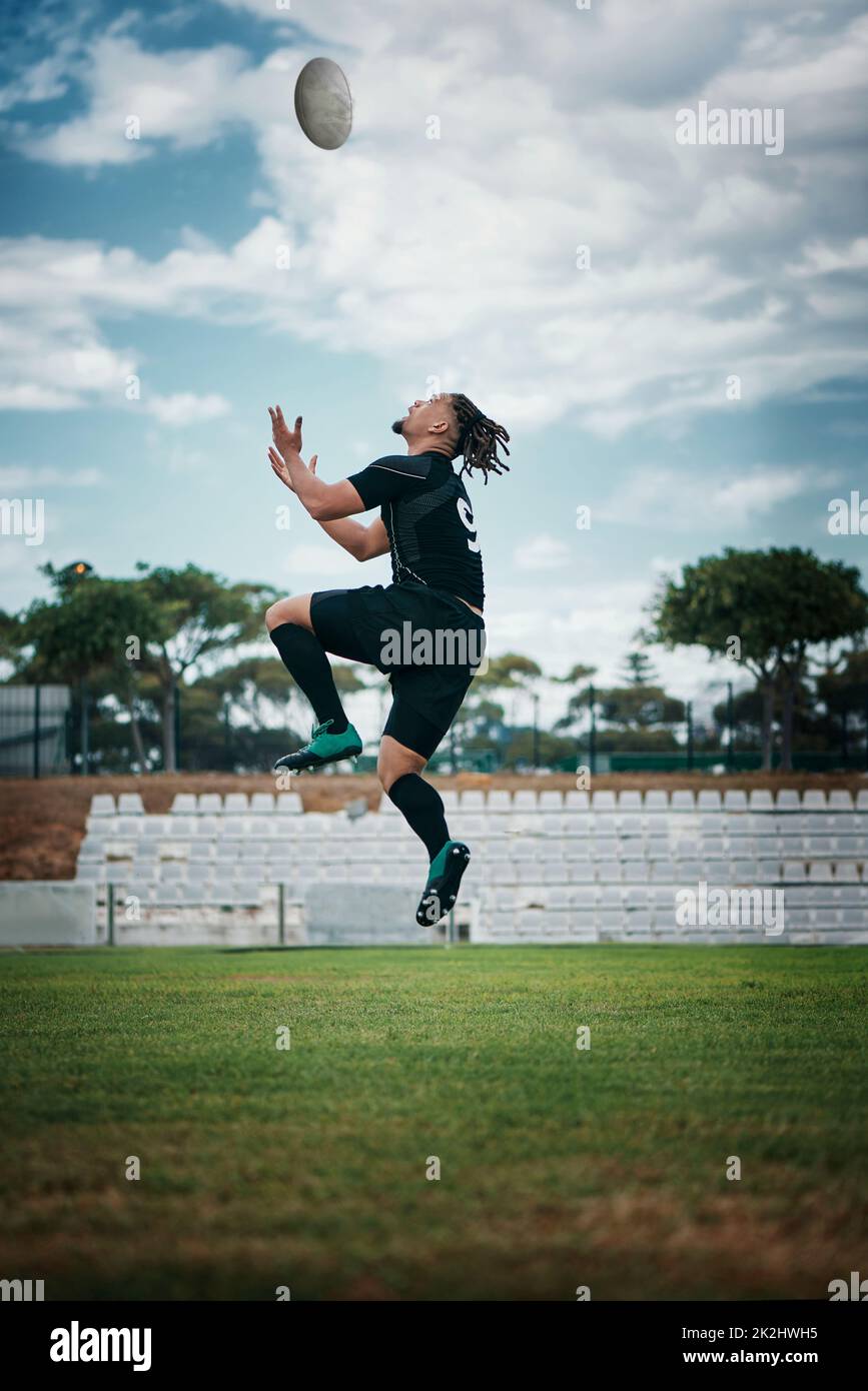 Train like a pro. Full length shot of a handsome young rugby player catching a ball mid-air on the field. Stock Photo