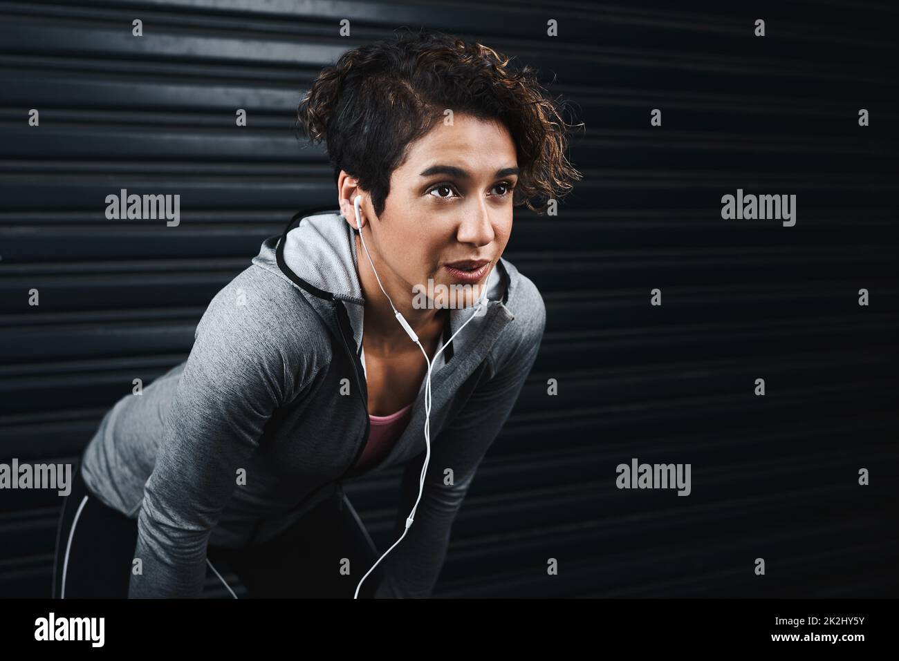I don't stop, I revitalise. Cropped shot of an attractive young woman wearing earphones and taking a break against a black background after exercising. Stock Photo