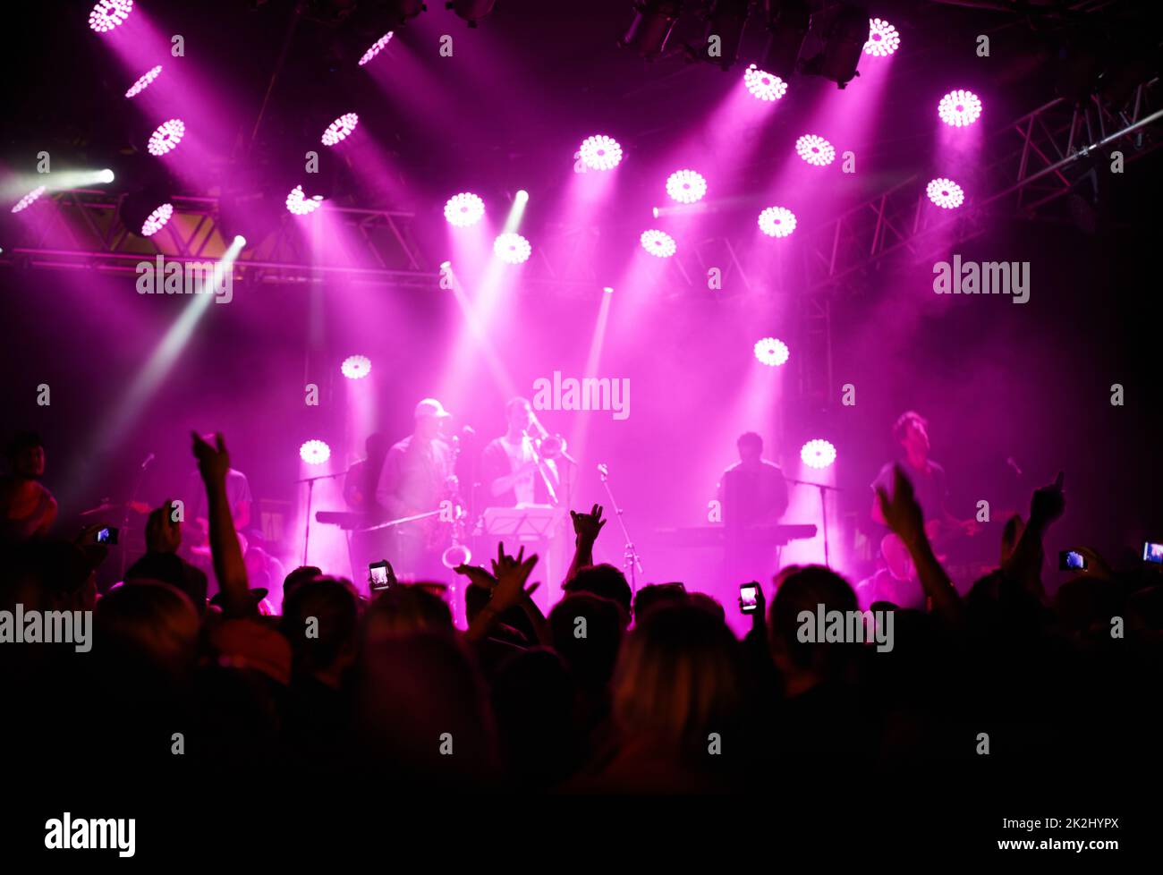 Sensational supporters. Rearview of an audience with hands raised at a music festival and lights streaming down from above the stage. Stock Photo