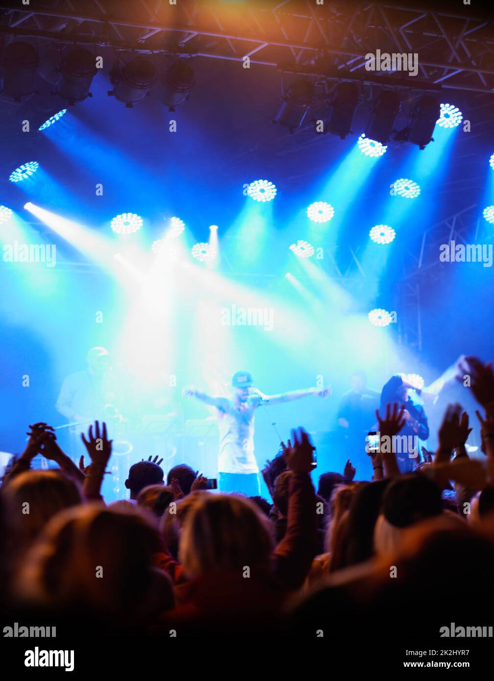 Praising the party people. Rearview of an audience with hands raised at a music festival and lights streaming down from above the stage. Stock Photo