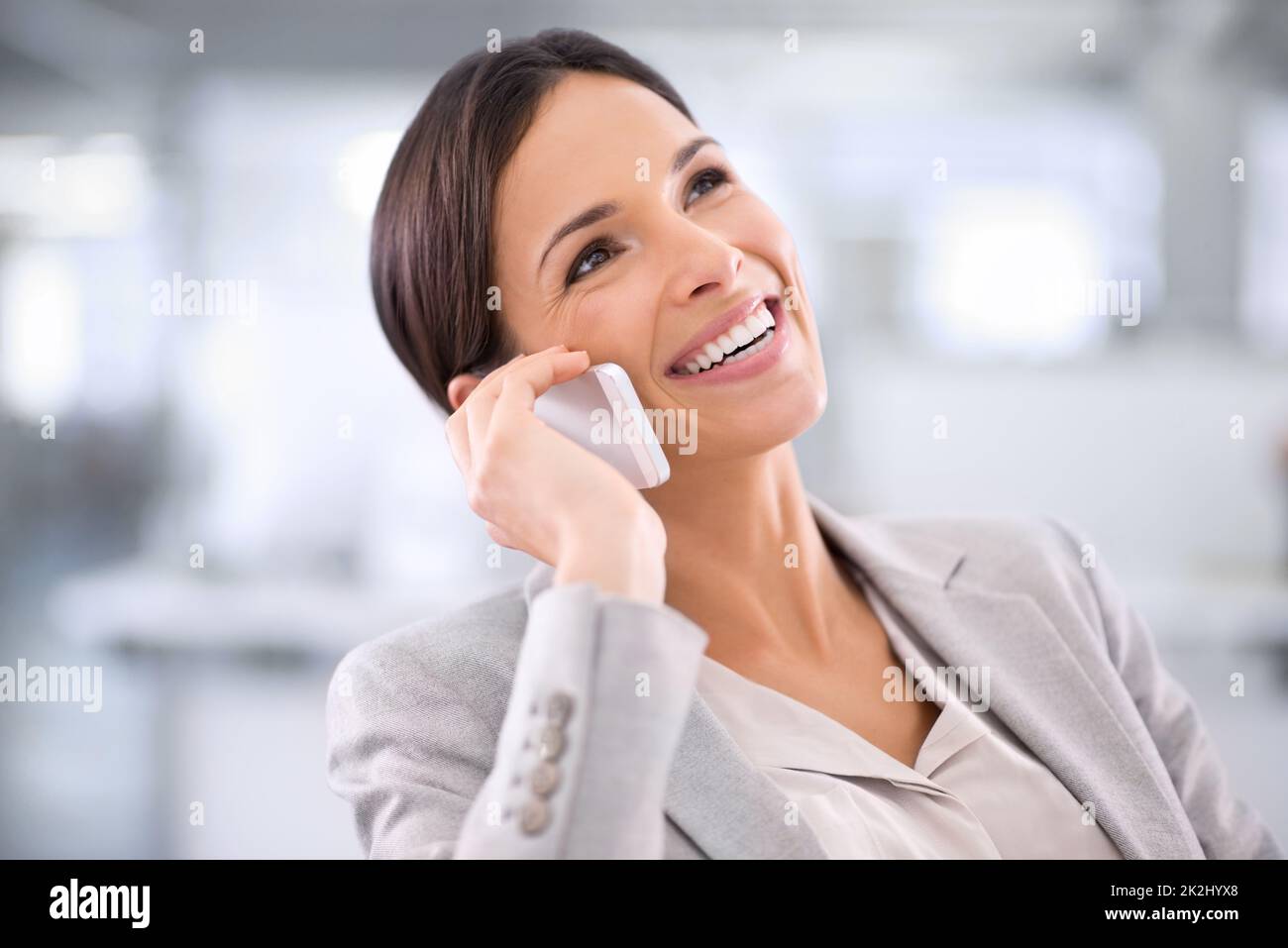 She's always available. Shot of a woman using a cellphone while sitting at a desk in an office. Stock Photo