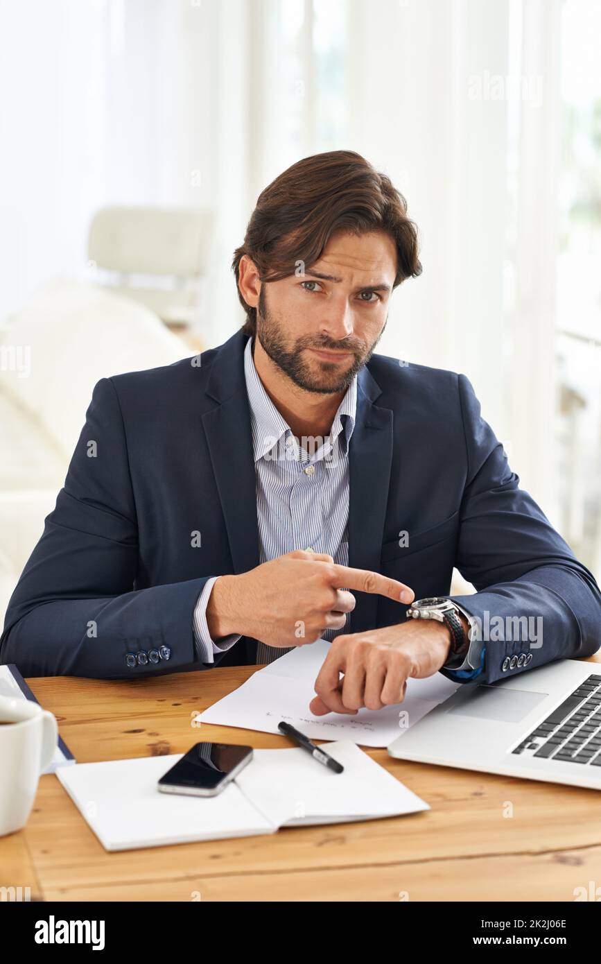 Punctuality is crucial in this office. A handsome businessman pointing to his watch while at his desk. Stock Photo