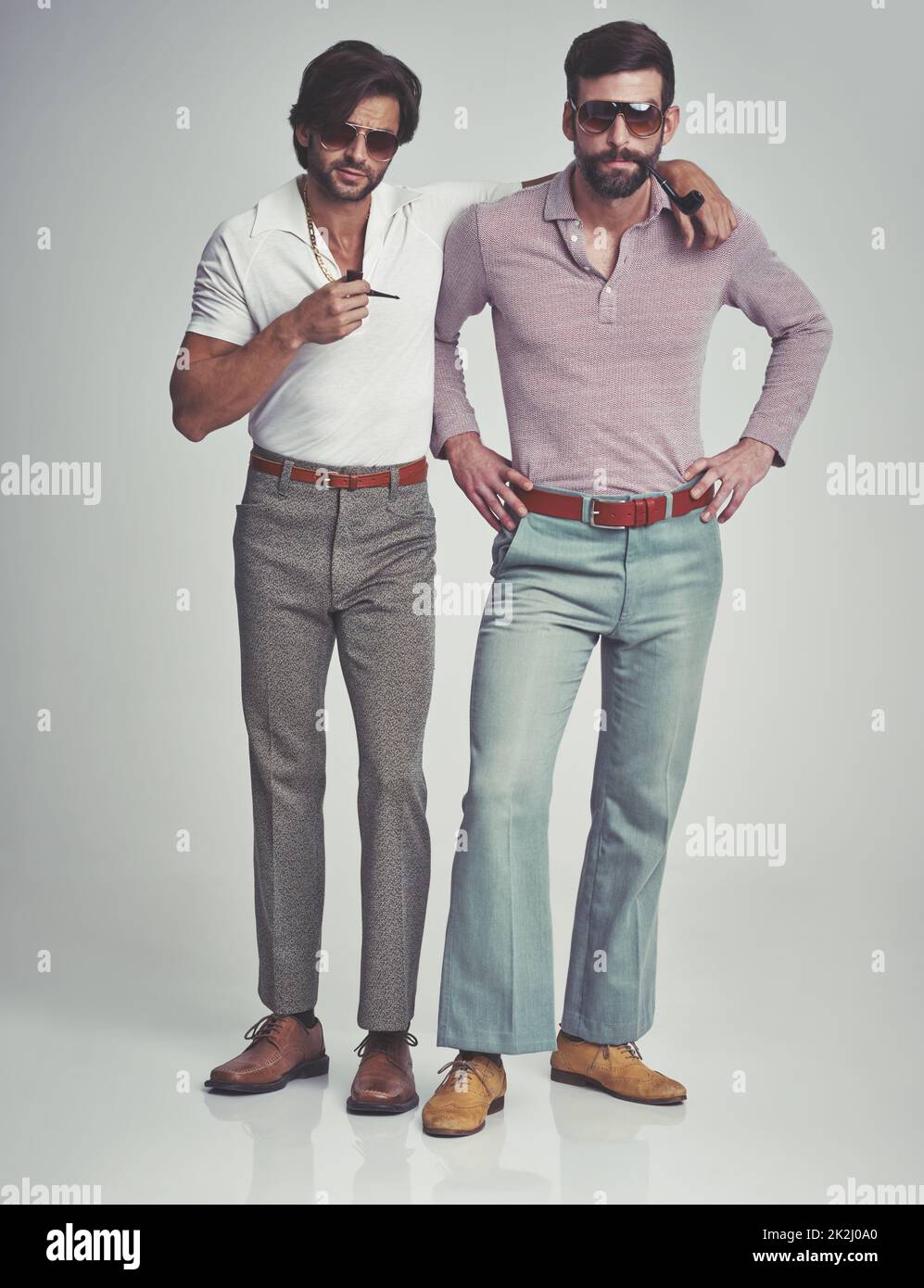Studio shot of two men standing together while wearing retro 70s wear and smoking pipes Stock Photo