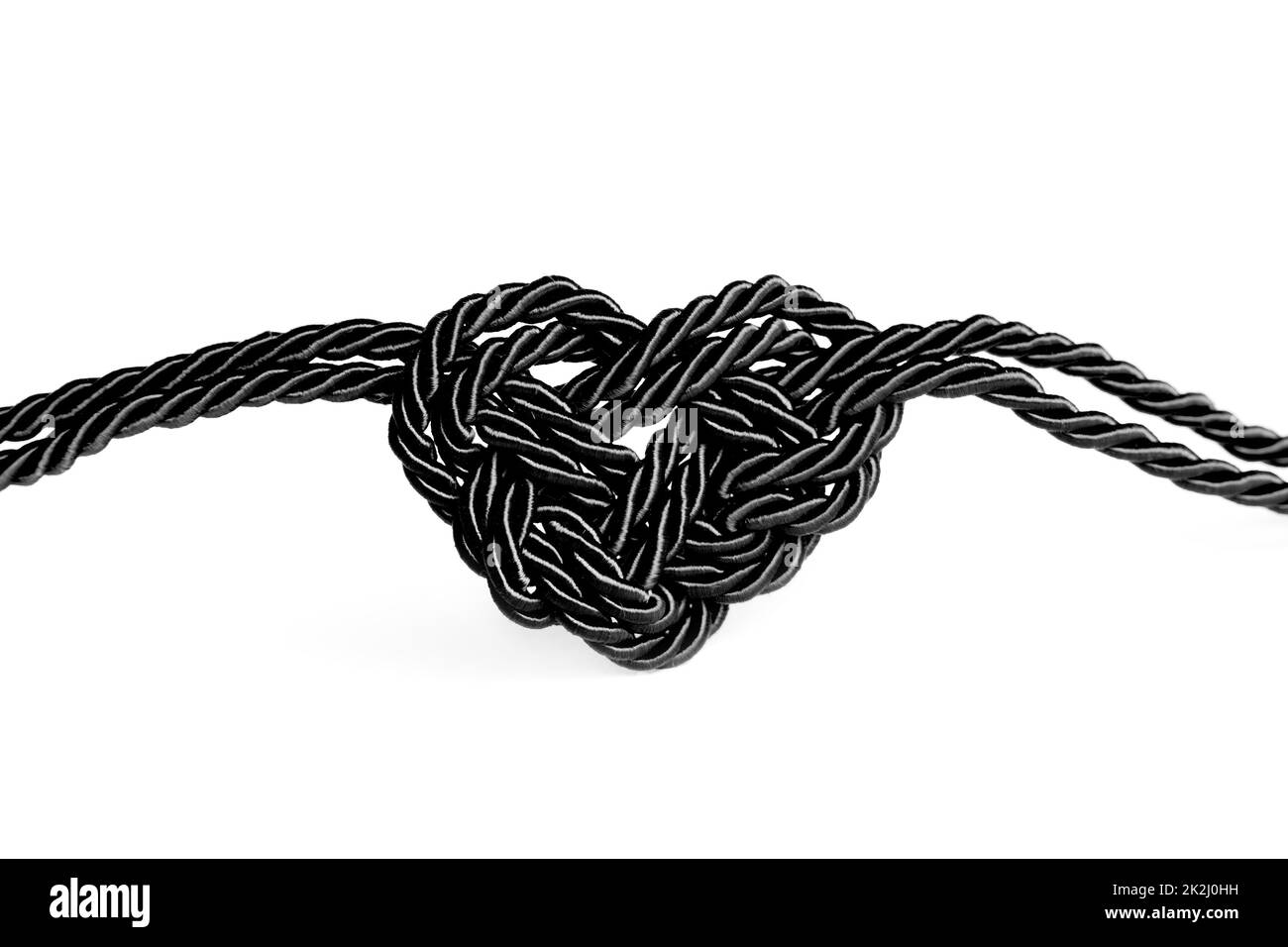 Heart shaped knot made from black braided cords isolated on white background. Mourning and grief concept. Stock Photo