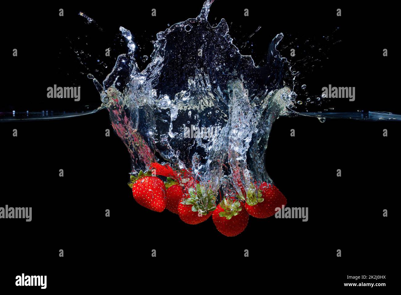 Bunch of fresh ripe strawberries dropped in water with splashes isolated on black background. Stock Photo