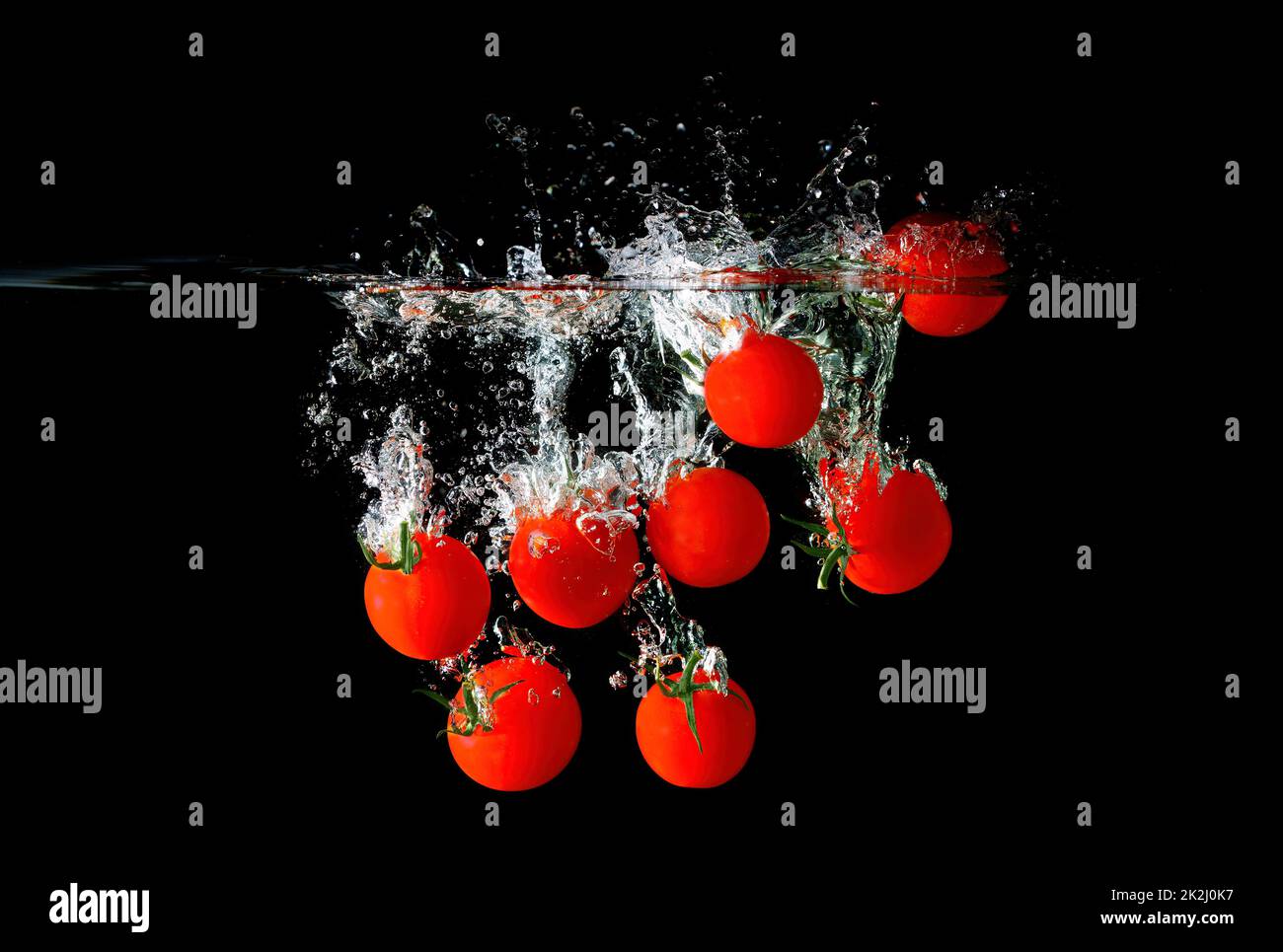 Ripe cocktail tomatoes dropped in water with splashes and bubbles isolated on black background. Stock Photo