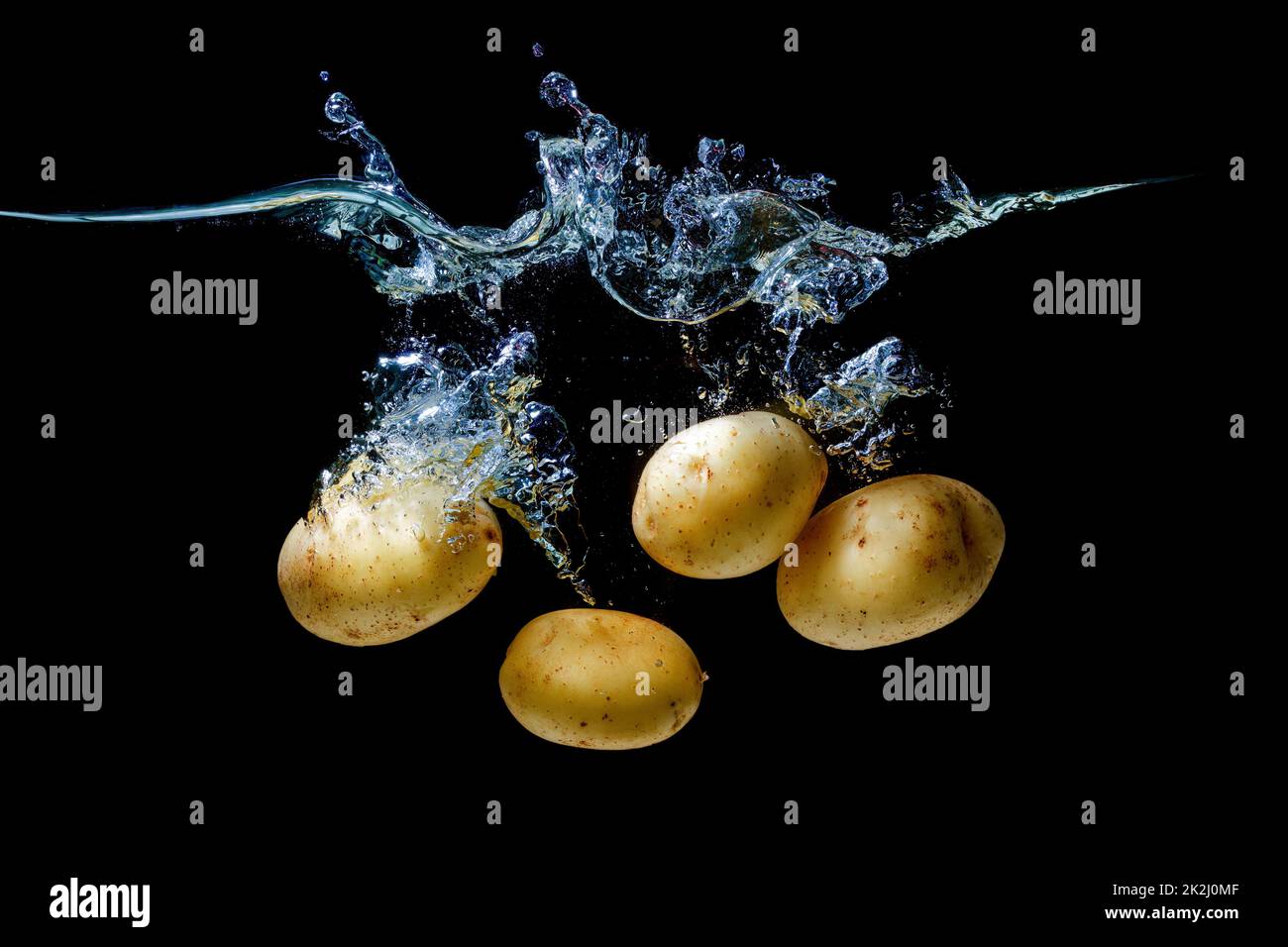 Bunch of fresh potatoes sinking underwater with splashes on black. Stock Photo