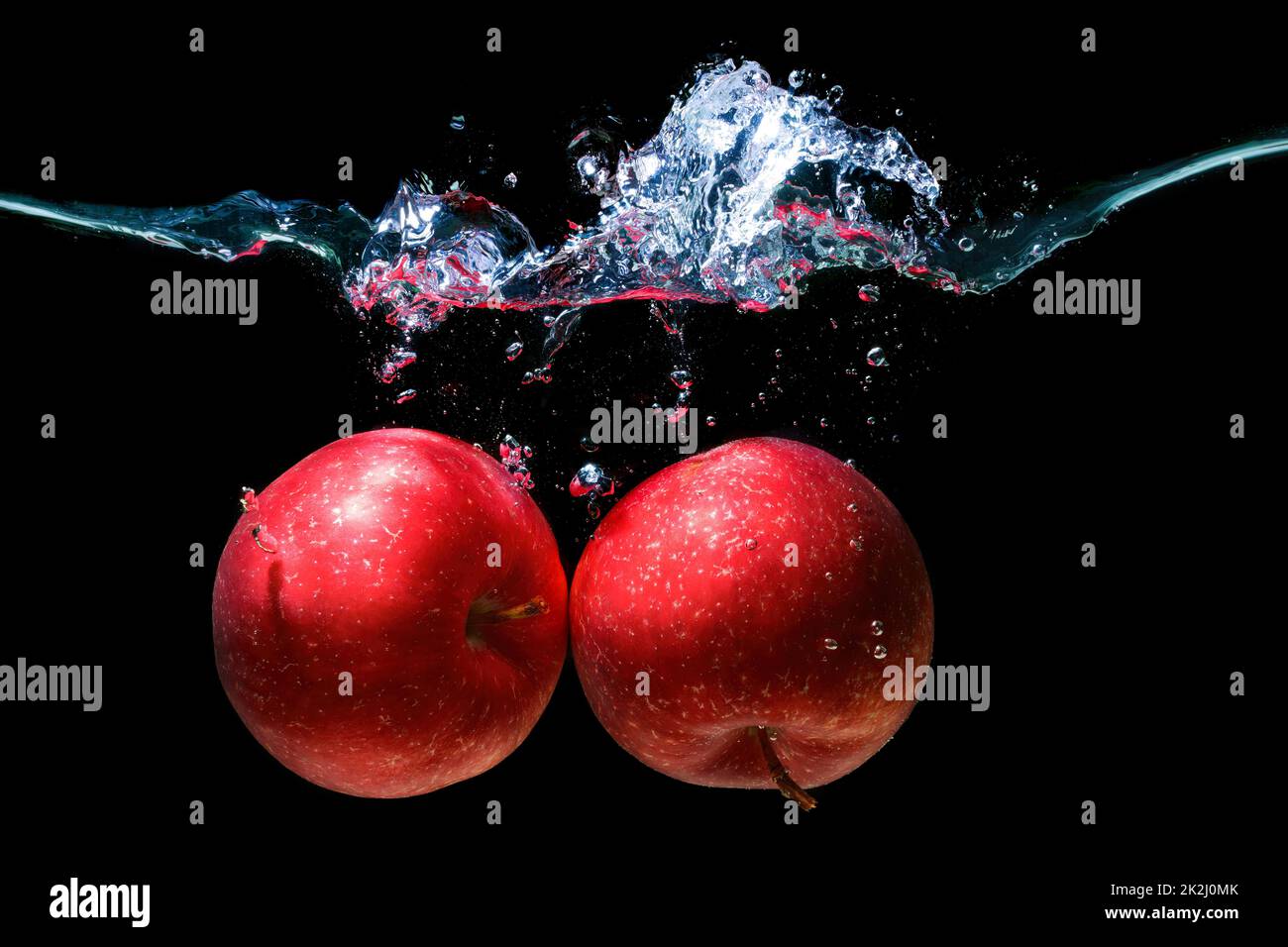 Close-up of two red apples thrown underwater with splashes on black. Stock Photo