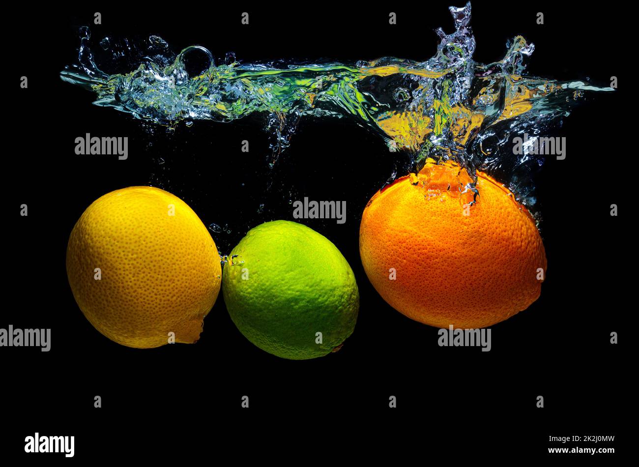 Lemon, kiwi and orange dropped in water with splashes isolated on black background. Stock Photo