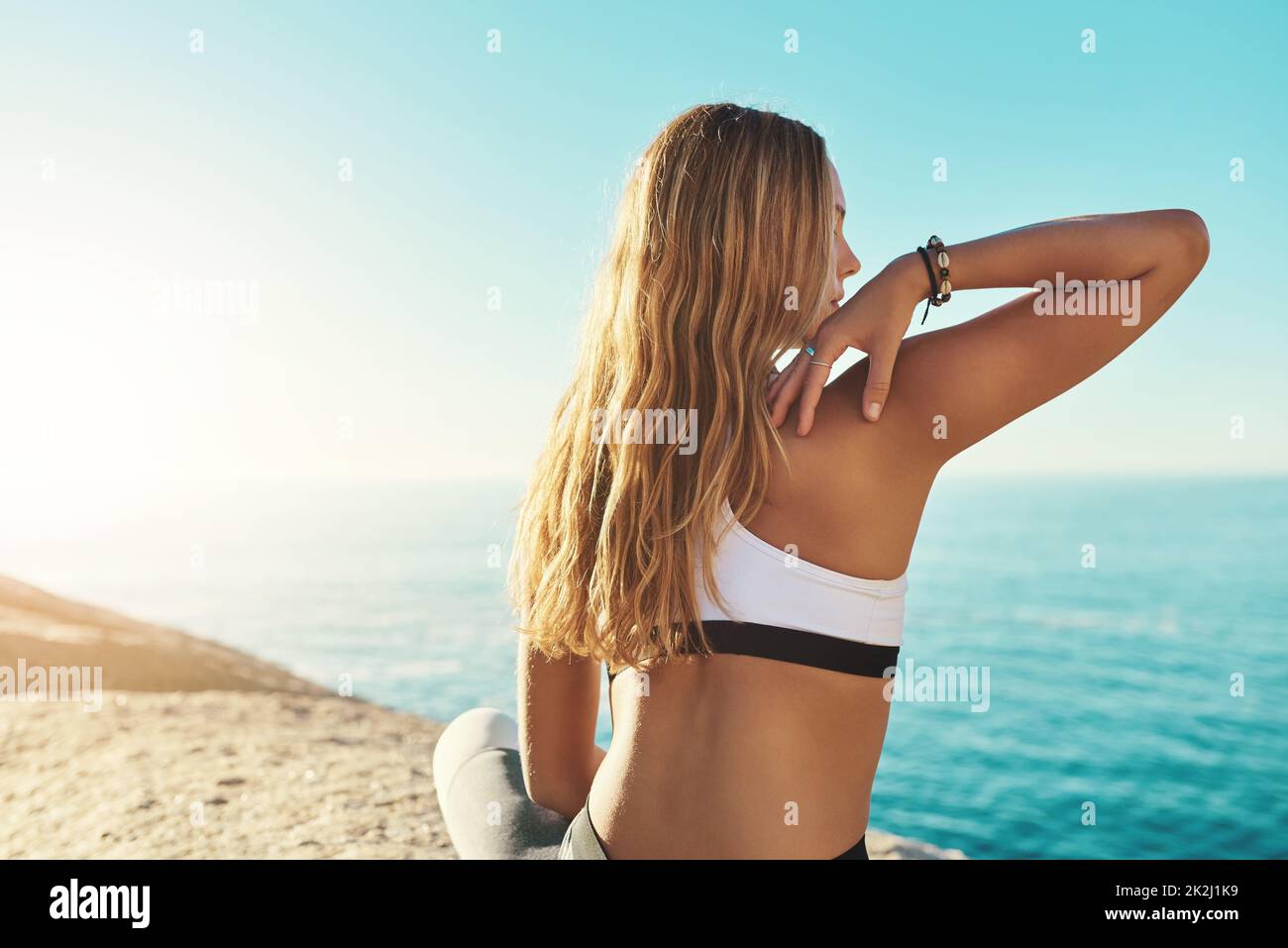 Be out there. Rearview shot of a young woman practicing yoga on the beach. Stock Photo