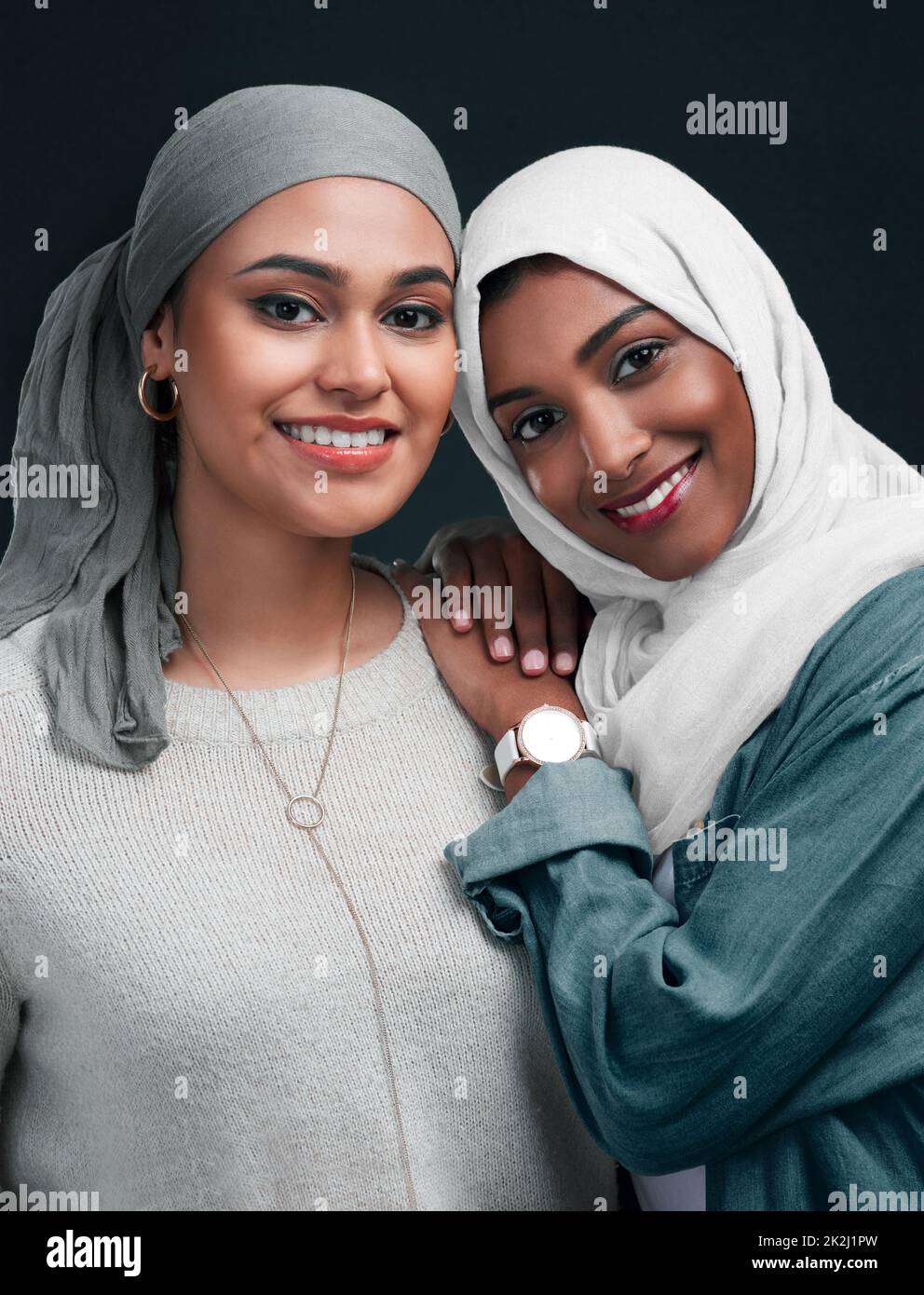 Friends until the end. Cropped shot of two attractive young women wearing hijabs and standing close together against a black background in the studio. Stock Photo