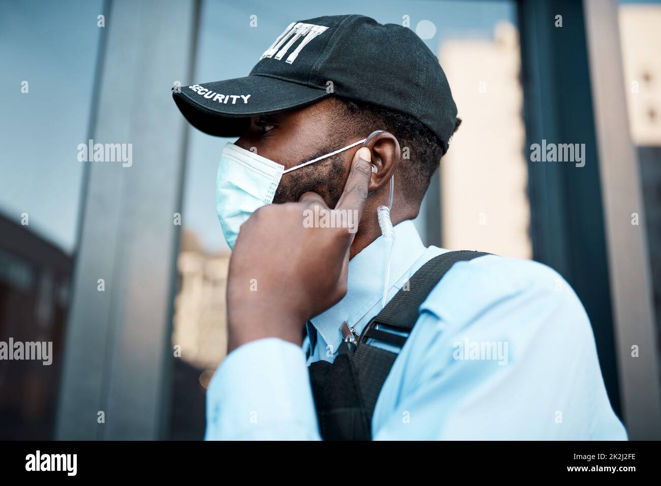 Swift action the first sign of trouble. Shot of a masked young security guard using an earpiece while on patrol outdoors. Stock Photo