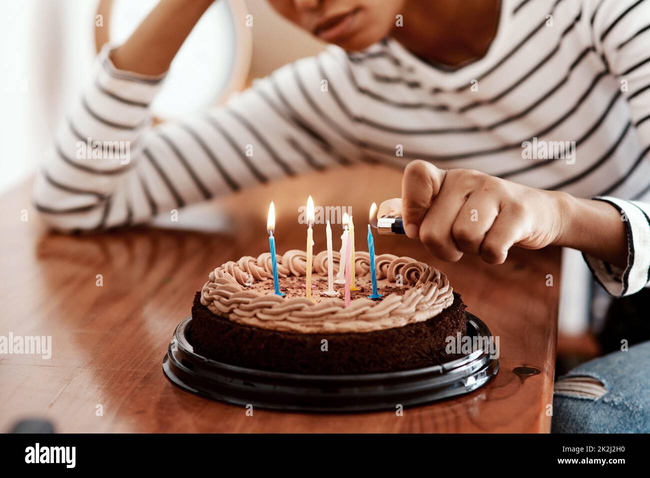 Birthdays in quarantine...not cool. Cropped shot of a woman lighting candles on a birthday cake at home and looking sad. Stock Photo