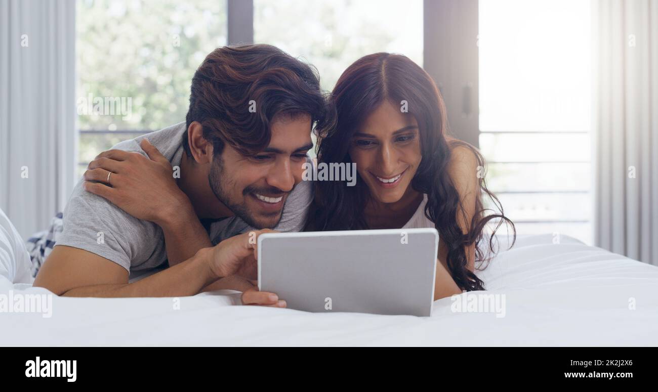 Lets spend the entire day in bed watching shows. Shot of a young attractive couple using a tablet together in the bedroom at home. Stock Photo