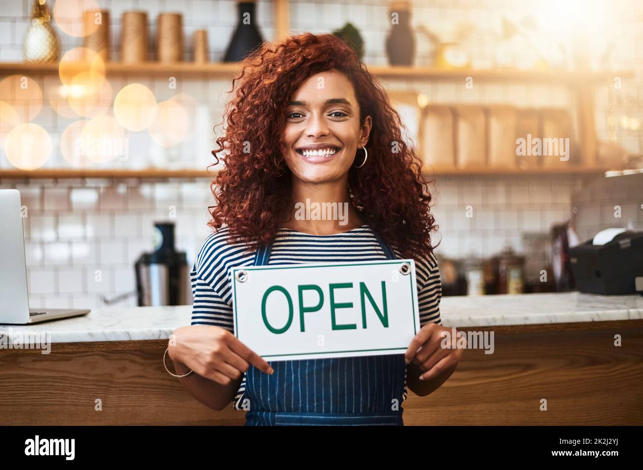 Service with a big smile. Portrait of a young woman holding up an open sign in her store. Stock Photo