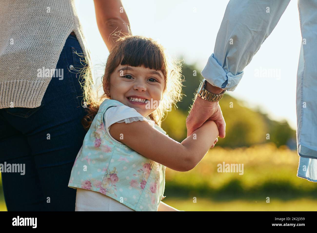 And off to the park we go. Portrait of an adorable and happy little girl holding her mother and fathers hands in the park. Stock Photo