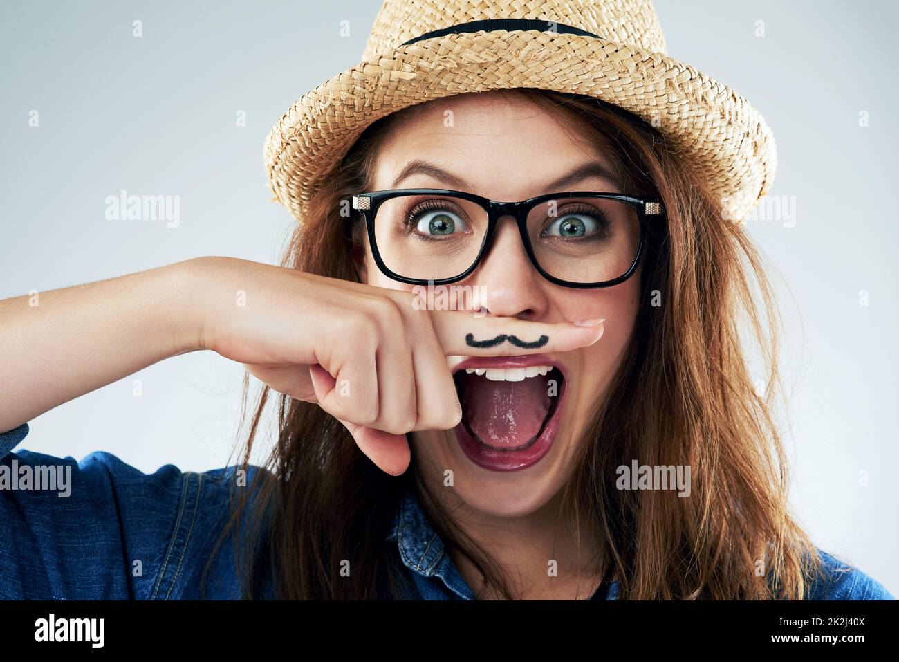 Dont take life too seriously. Studio portrait of a young woman holding her finger under her nose with a moustache drawn on it. Stock Photo