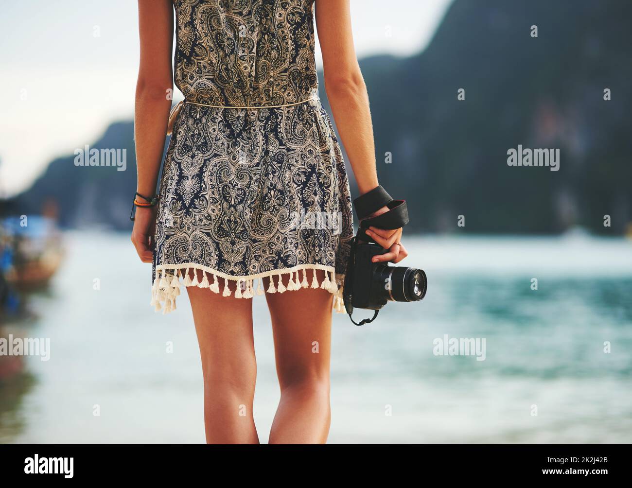 No moment goes uncaptured. Rear view shot of a young woman walking on the beach with a camera in hand. Stock Photo