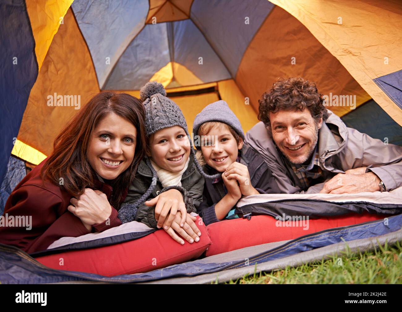 Family camping is family bonding. Portrait of smiling family of four relaxing in tent on a camping holiday. Stock Photo
