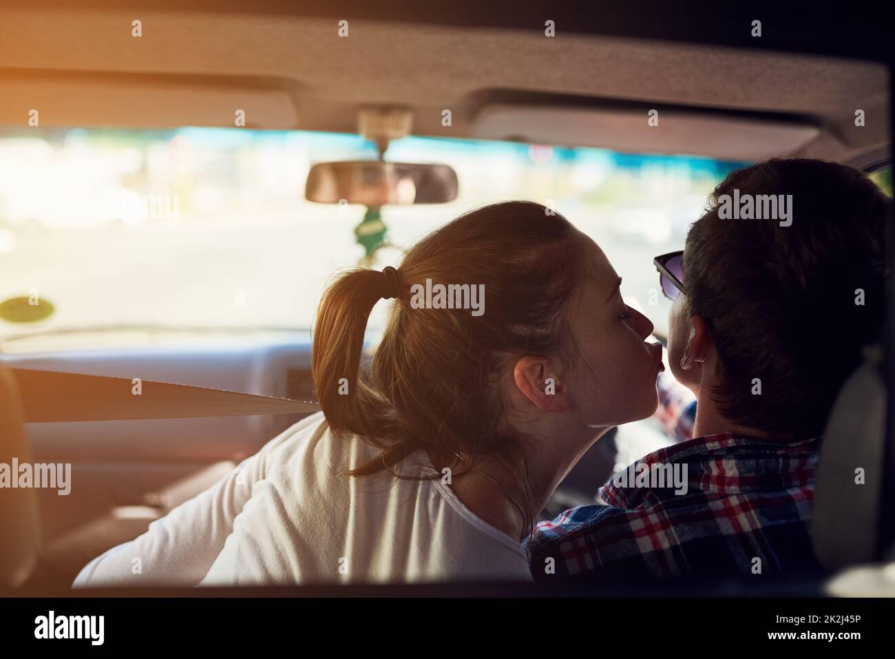 Some kisses cant wait. Rearview shot of a young woman kissing her boyfriend while he drives a car. Stock Photo